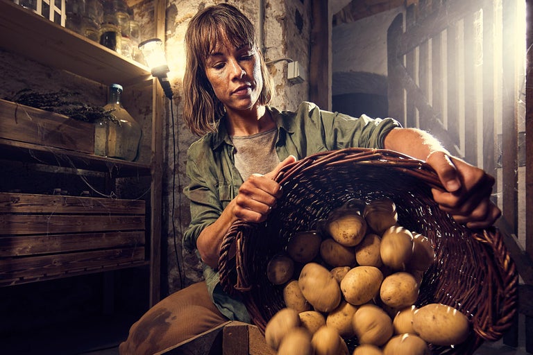 Femme tenant un panier de pommes de terre dans la cave.