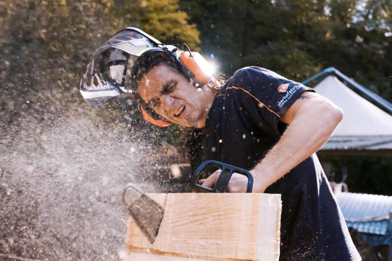 Mann sägt Holz mit einer Kettensäge mit Schutzkleidung