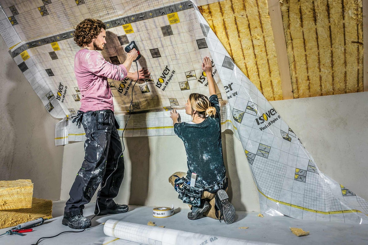 Deux personnes fixent un film pare-vapeur Isover sur un toit en pente.