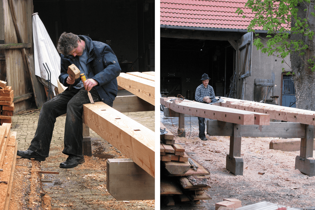 Deux artisans travaillent des poutres en bois avec des outils dans un atelier.