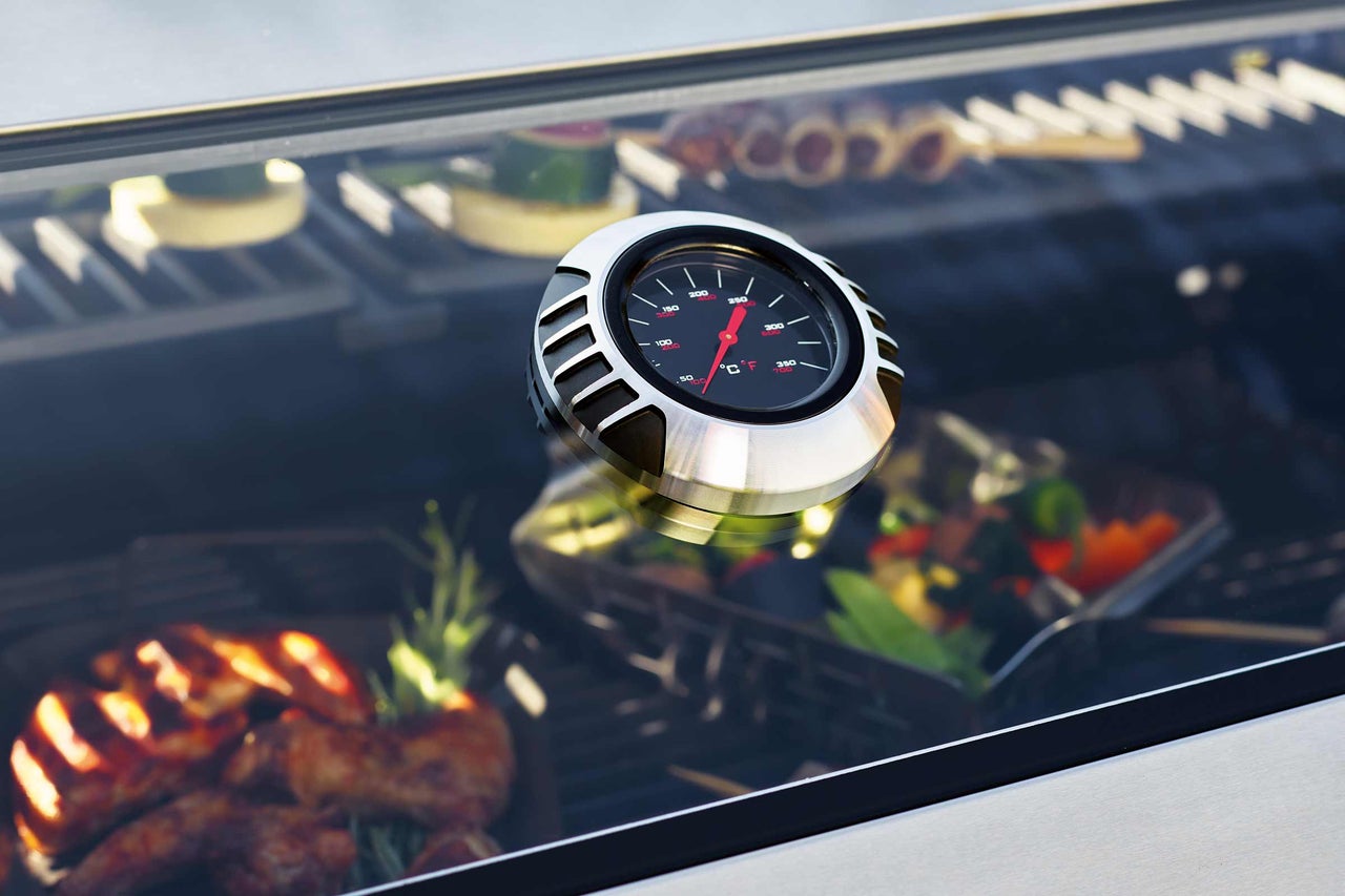 Gros plan d'un thermomètre de gril avec des aliments en arrière-plan.