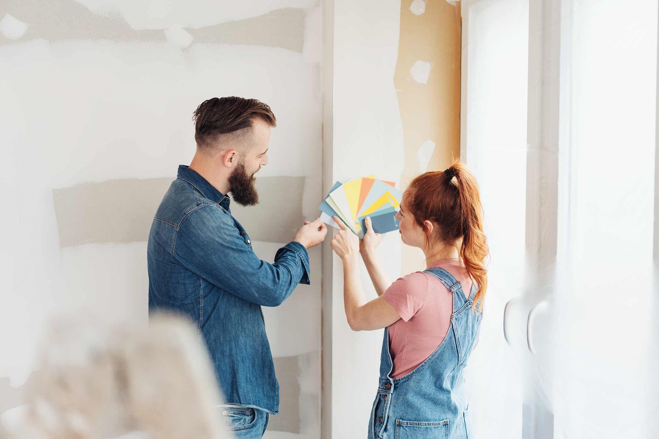 Un couple choisit des échantillons de couleurs de peinture devant un mur inachevé pour la rénovation.