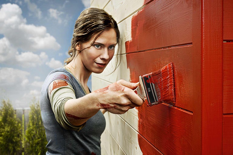 Femme peignant un mur en bois avec un pinceau et de la peinture pour bois