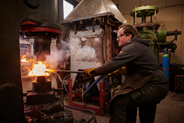 Schmied bearbeitet glühendes Metall mit einer Schmiedepresse in einer Werkstatt