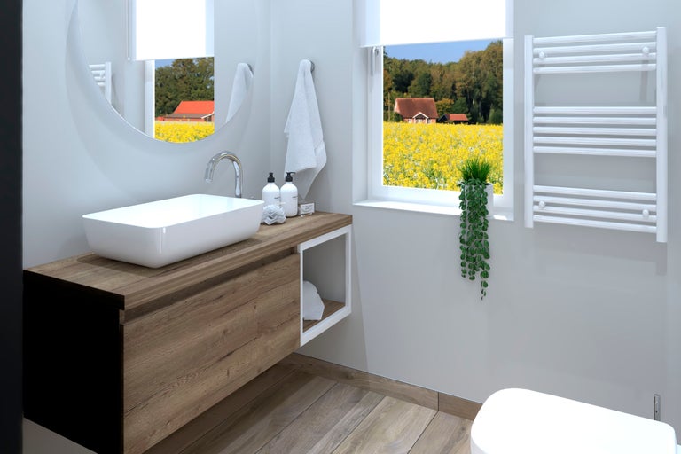 Badezimmer mit Waschtisch, Spiegel, Handtuchheizkörper und Fenster mit Blick in die Natur