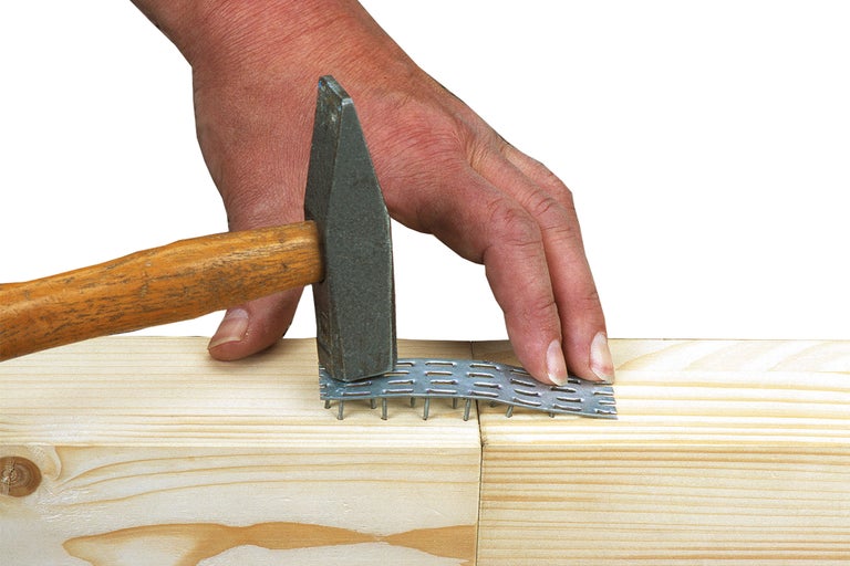 Un marteau enfonce une plaque à clous dans deux pièces de bois.