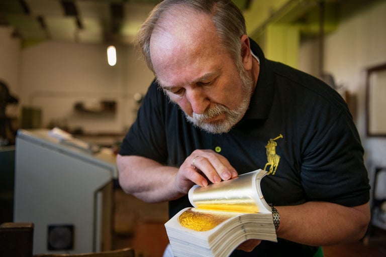 Ein Mann hantiert mit Blattgold in einem Buch.