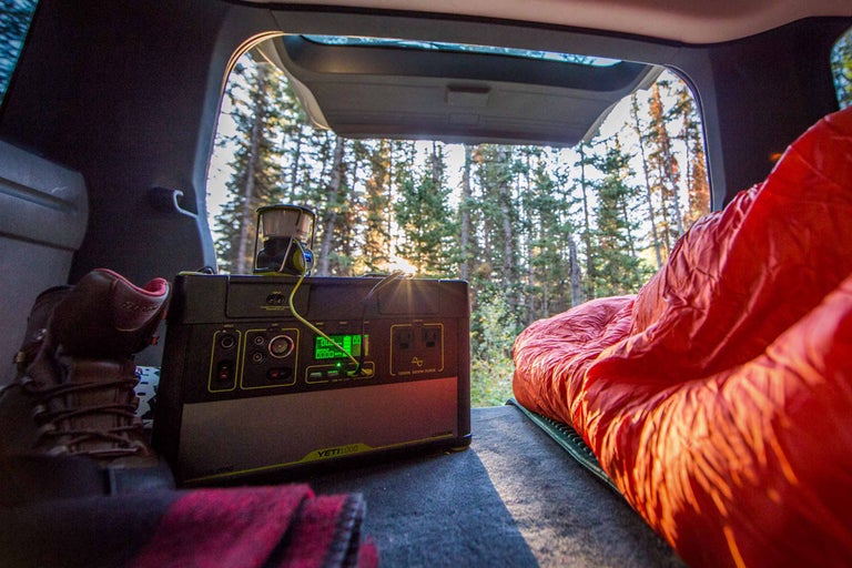 Szene im Kofferraum eines Autos mit tragbarem Goal Zero Yeti 1000 Lithium-Kraftwerk, Schlafsack, Schuhen und Blick auf Bäume.