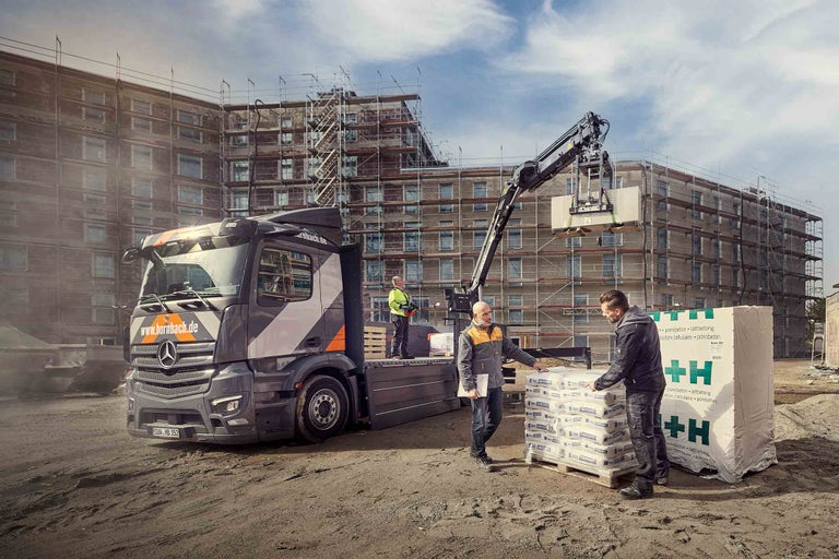 Scène sur un chantier avec camion, ouvriers du bâtiment et matériaux de construction devant un gros œuvre.