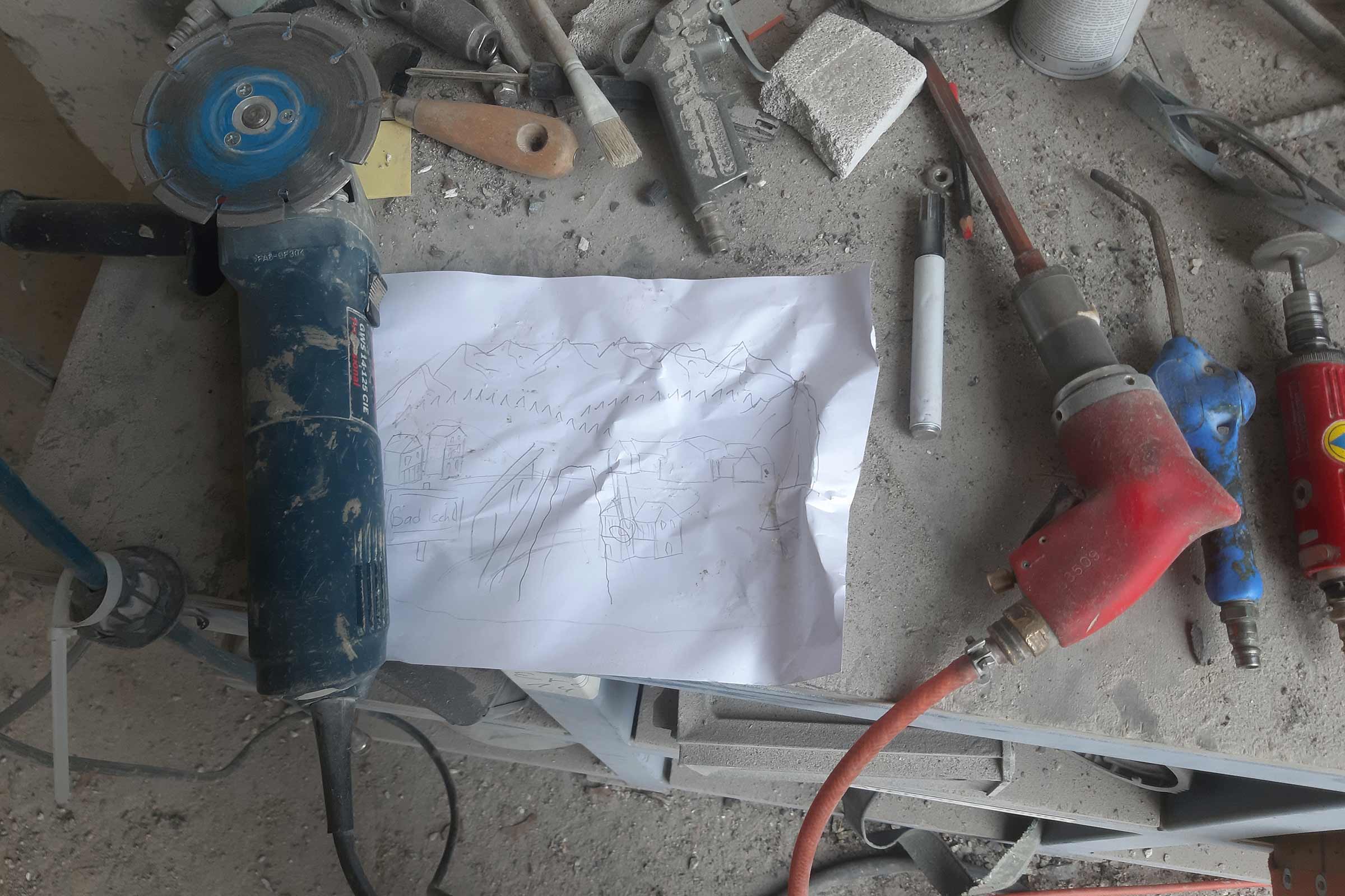 Eine Schleifmaschine, eine Skizze und andere Werkzeuge auf einer Werkbank.