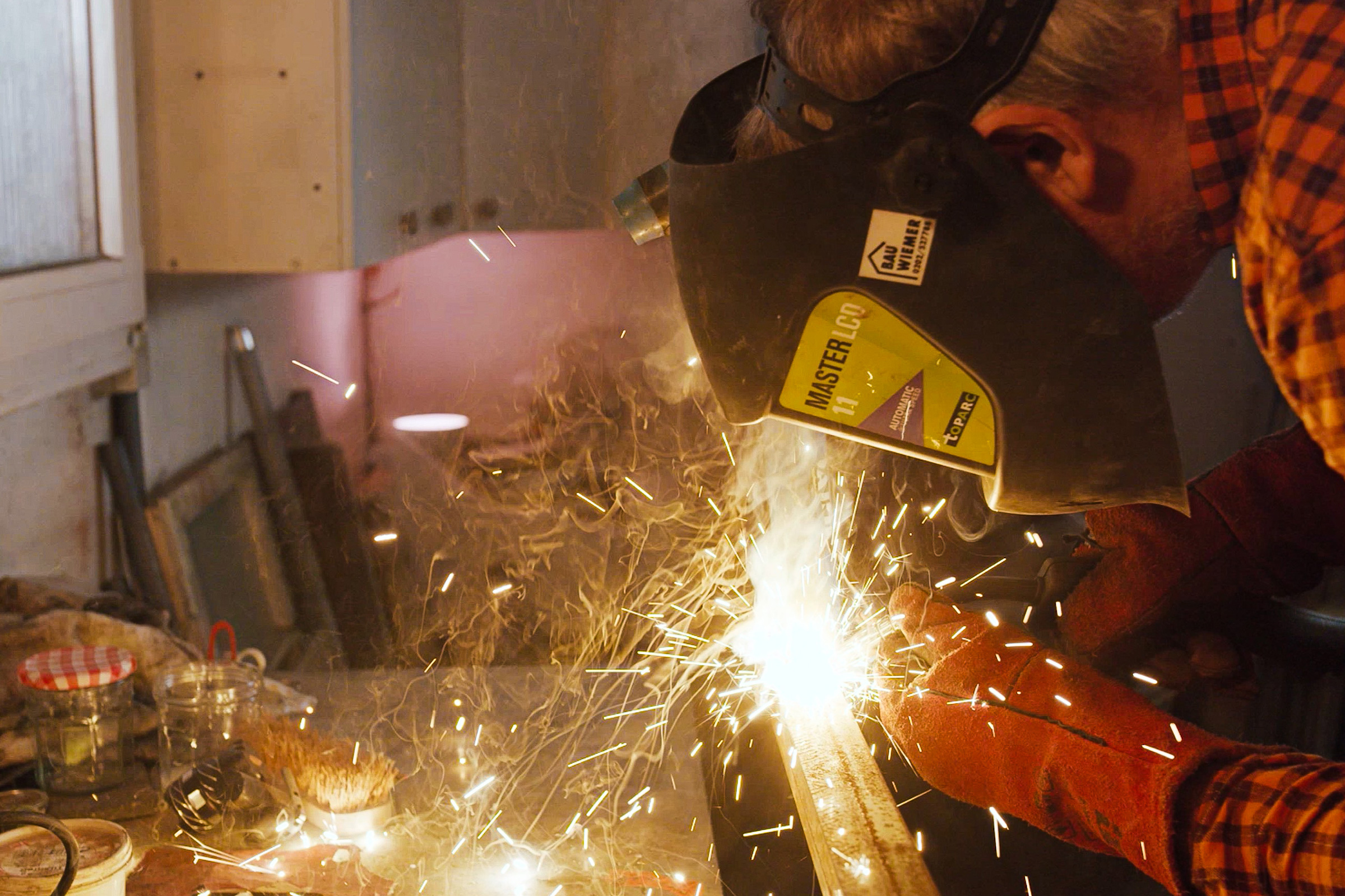 Schweißer mit Schweißhelm bei der Arbeit in einer Werkstatt