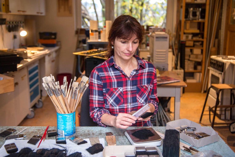 Frau reinigt Pinsel in Werkstatt mit Arbeitsmaterialien