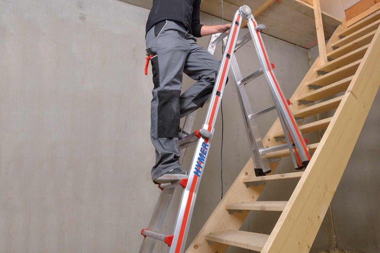 Mann auf Mehrzweckleiter von Hymer im Innenraum, neben Holztreppe