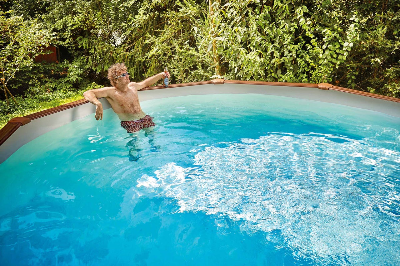 Un homme se détend dans une piscine tubulaire avec une boisson dans le jardin.
