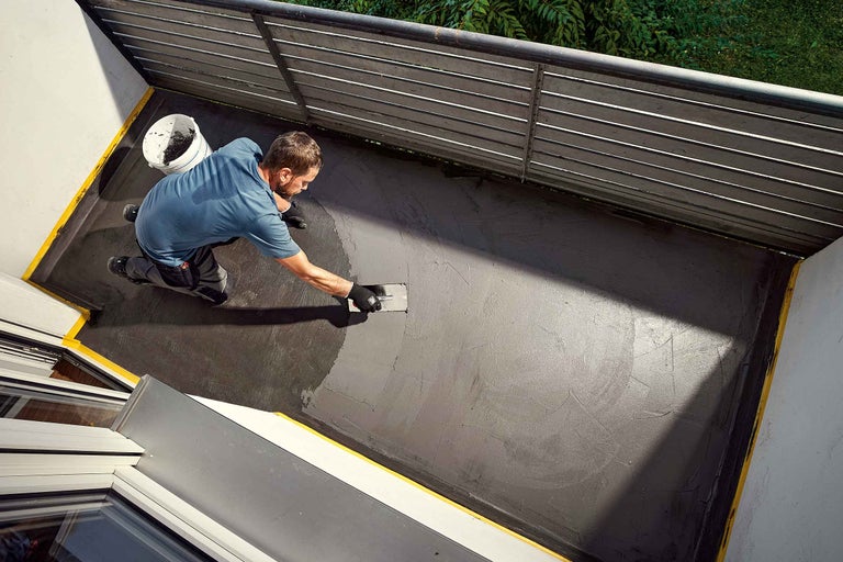 Un homme applique un revêtement gris avec une lisseuse sur un balcon