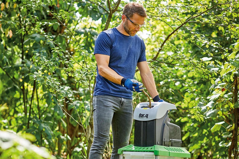 Un homme utilise un broyeur de branches dans le jardin.