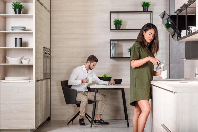 Helle Küche mit Mann am Tisch und Frau beim Kaffeekochen