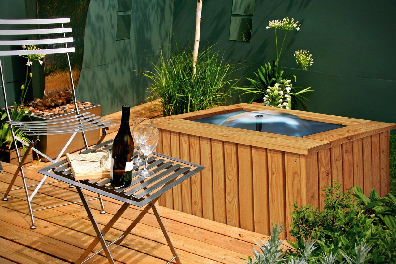 Scène avec mobilier de jardin, bain à remous, bouteille de vin et verres sur une terrasse en bois