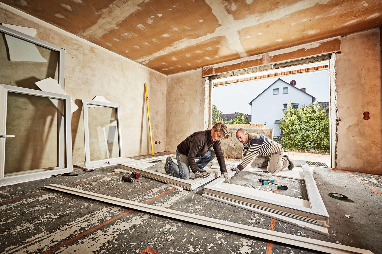 Zwei Personen montieren ein Fenster in einem Raum, der renoviert wird.