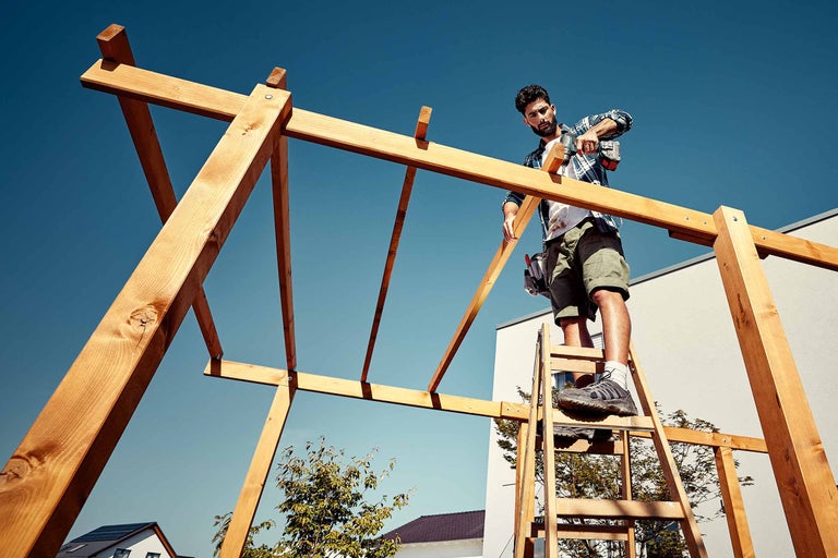 Un artisan assemble une construction en bois avec une visseuse sans fil dans le jardin.