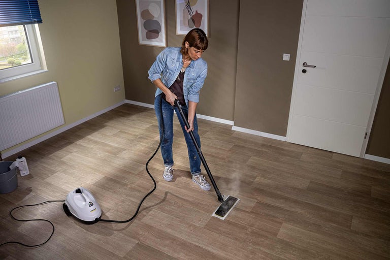 Femme nettoie le sol avec un nettoyeur à vapeur dans une pièce avec parquet
