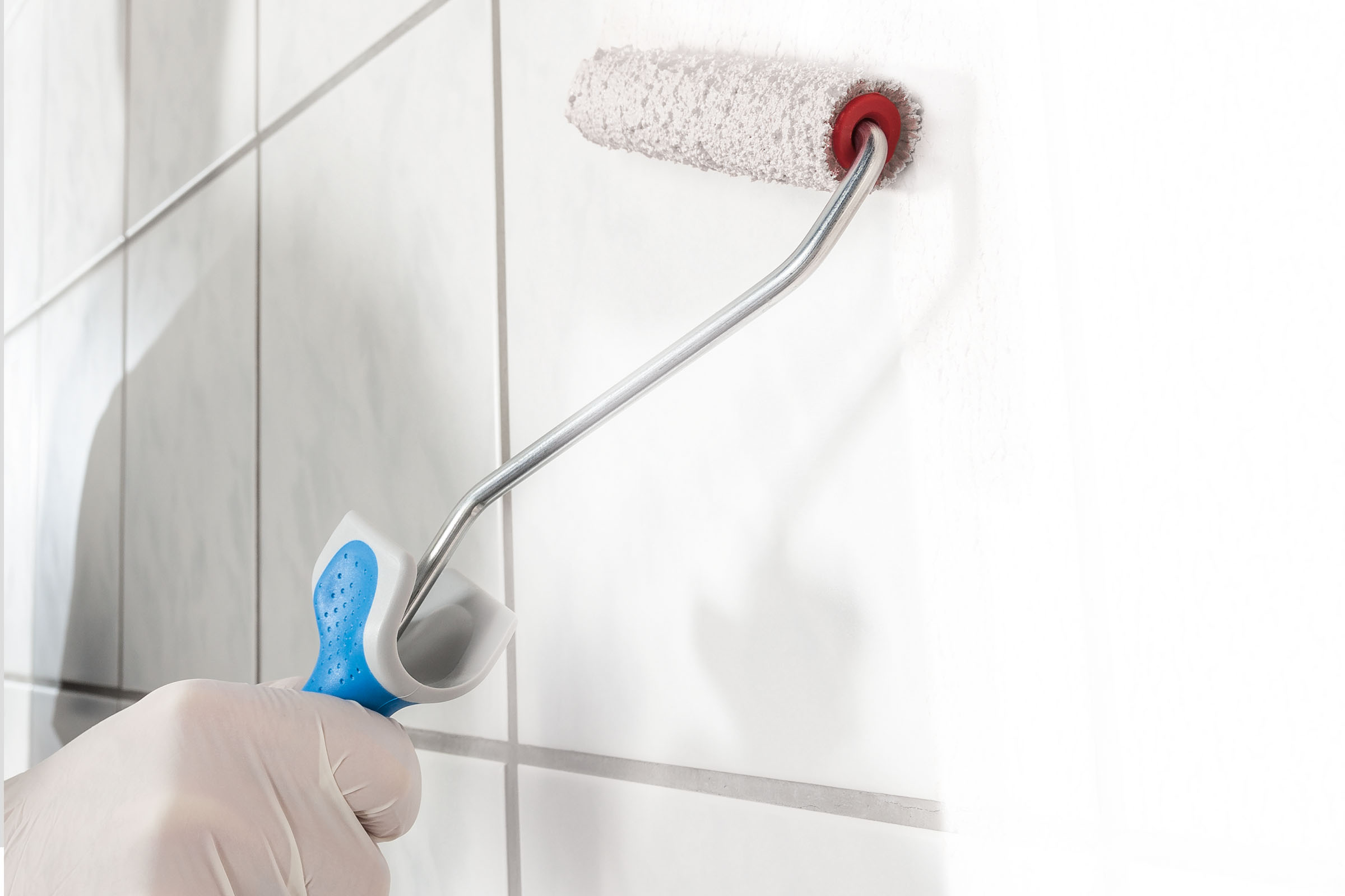 Eine Person mit Handschuhen verwendet eine Farbwalze zum Streichen einer Wand.