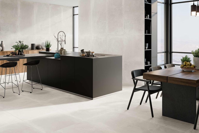 Pièce lumineuse avec carrelage grand format au sol et au mur, îlot de cuisine et table à manger.