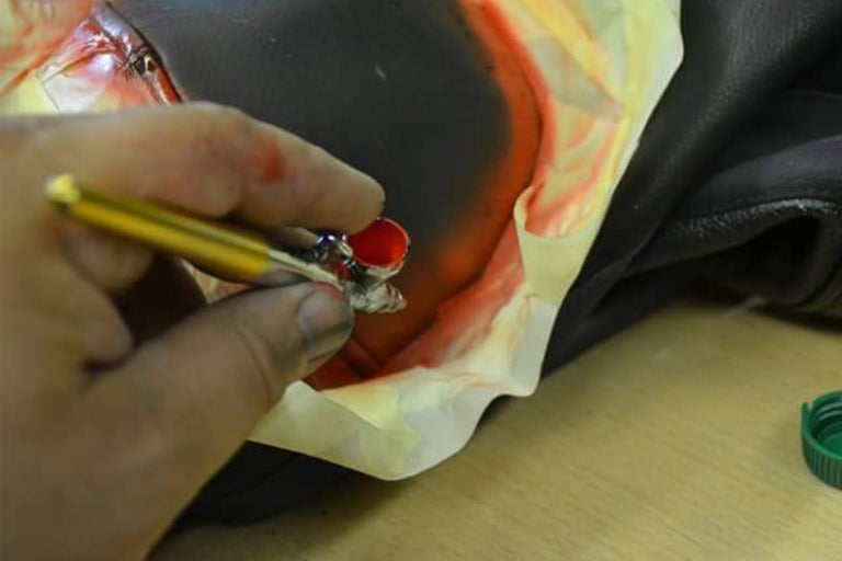 Detailaufnahme einer Hand, die mit einer Airbrush Pistole Farbe auf ein Objekt sprüht