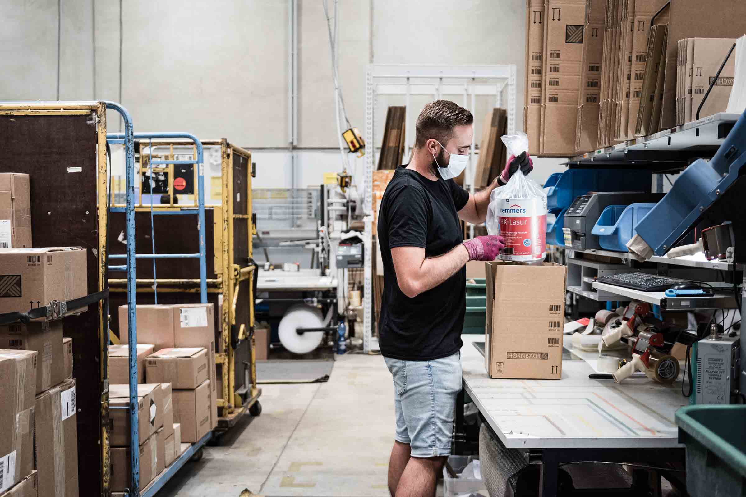 Un employé de l'entrepôt emballe la lasure pour bois Remmers dans un carton pour l'expédition.