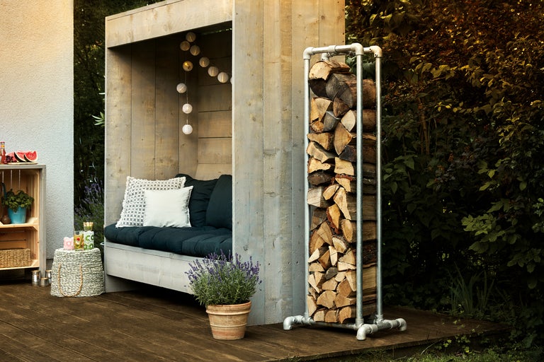 Support à bois métallique avec bûches à côté d'une cabane en bois avec des sièges sur une terrasse