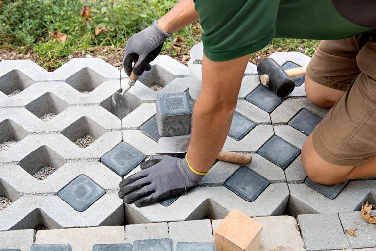 Un homme pose des dalles alvéolées avec des pavés comme remplissage