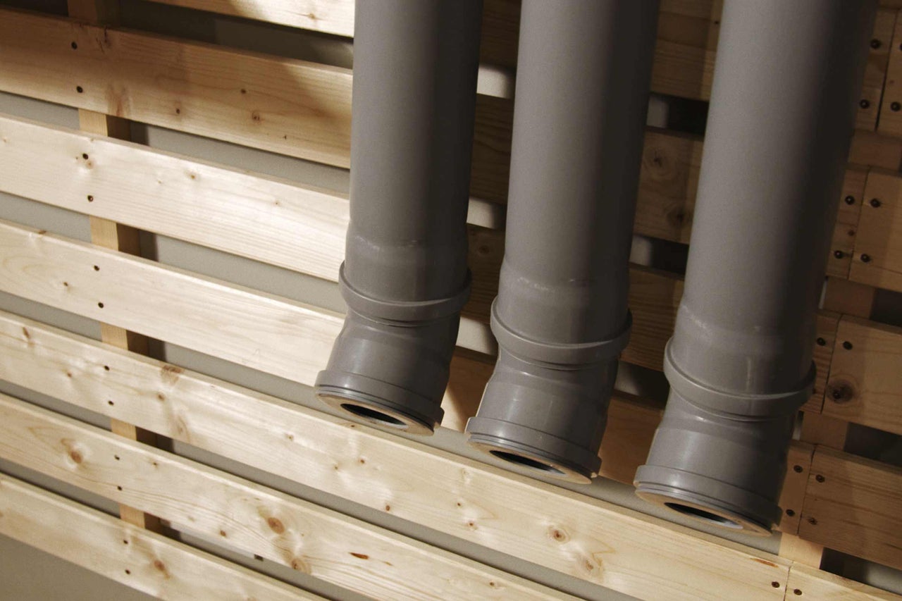 Trois tuyaux en plastique gris devant une construction en bois