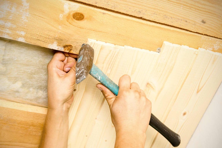Eine Person nagelt Holzpaneele mit einem Hammer an einer Holzwand.