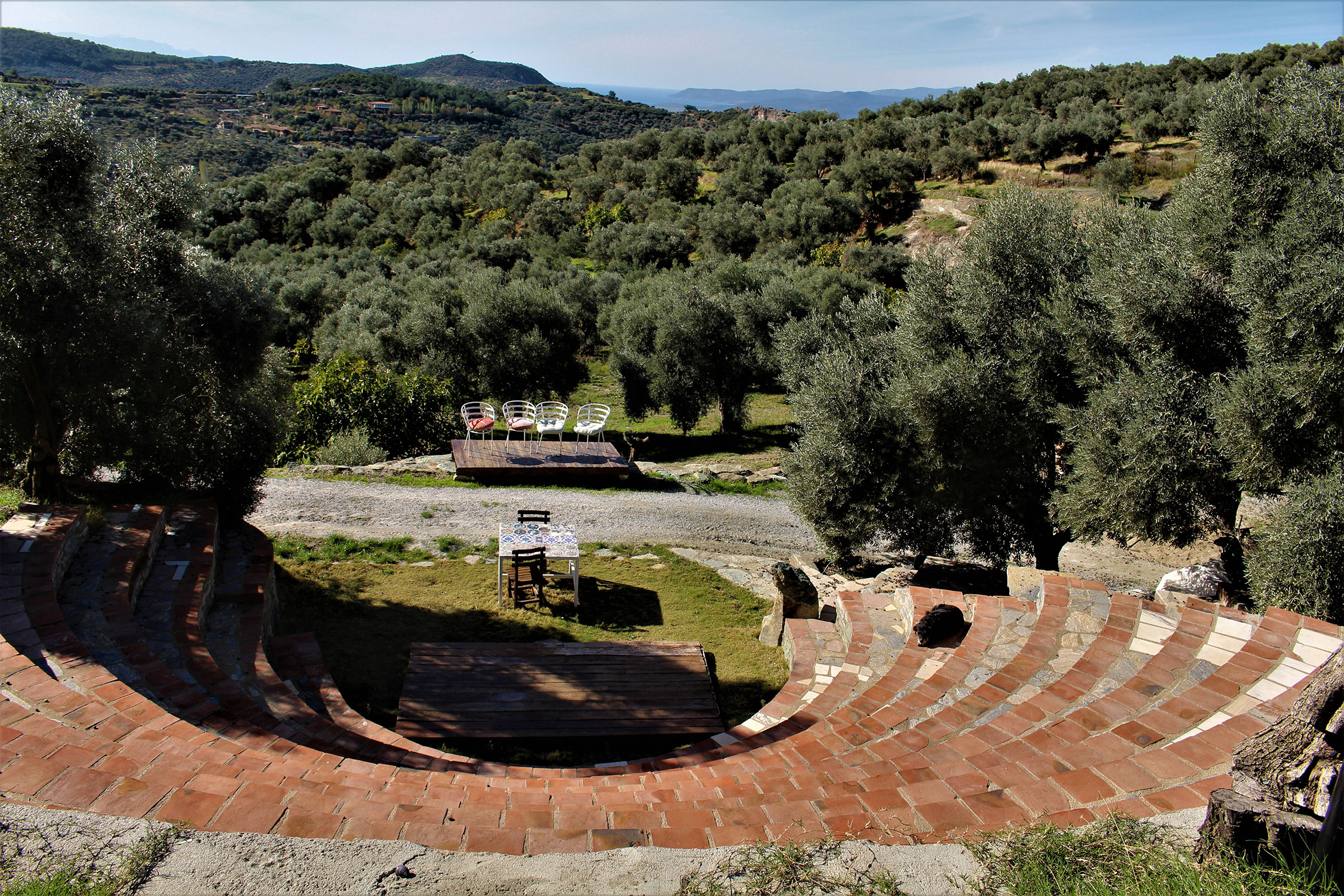 Amphitheater mit Ziegelstufen und Blick auf eine bewaldete Landschaft mit Tischen und Stühlen