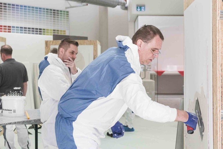 Personen tragen Schutzkleidung und tragen Putz auf eine Wand auf.