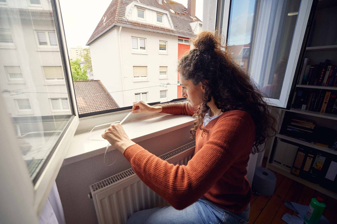 Une femme fixe un ruban d'étanchéité sur un cadre de fenêtre pour l'étanchéité des fenêtres