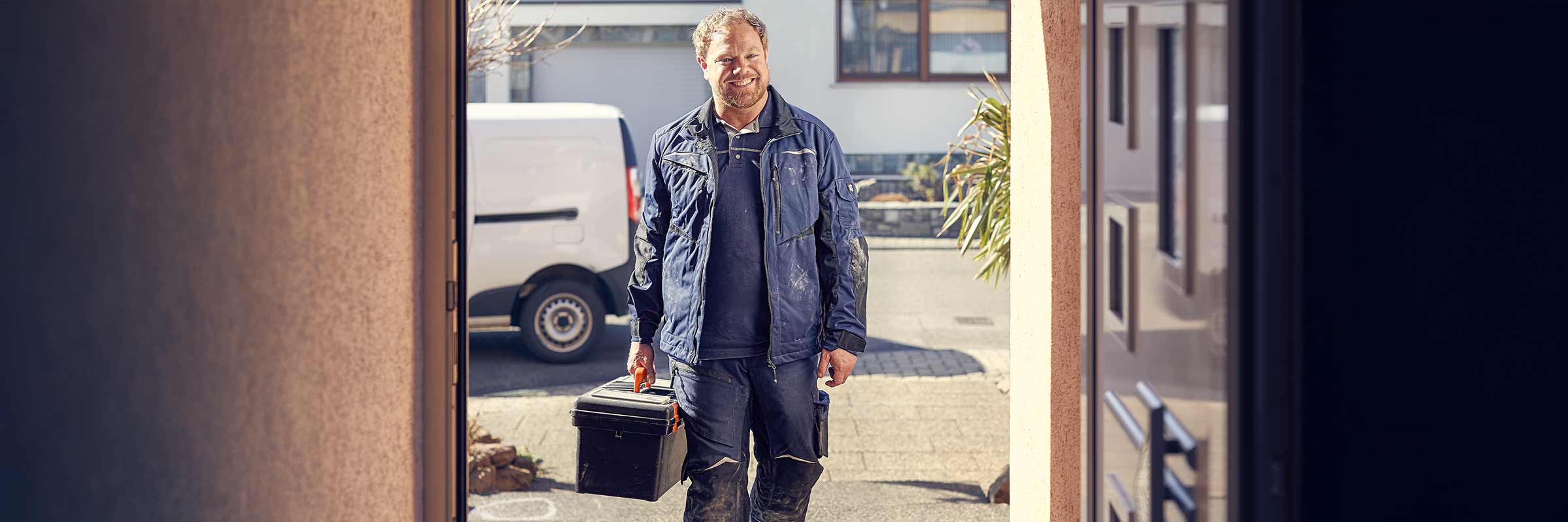 Artisan avec une boîte à outils devant une maison