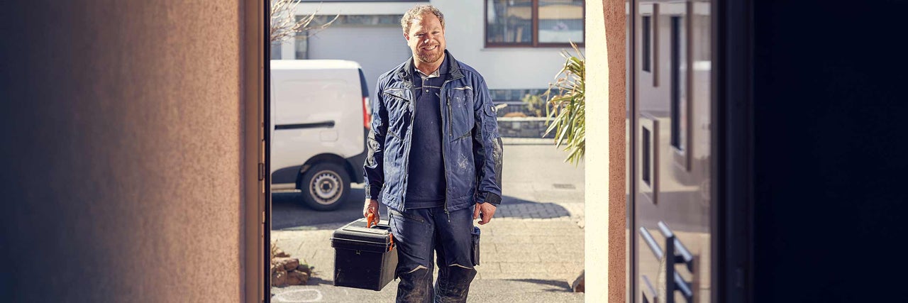 Handwerker mit Werkzeugkoffer vor einem Haus