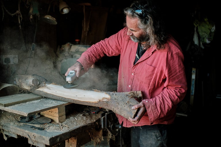 Ein Mann schleift ein Stück Holz mit einer Schleifmaschine in einer Werkstatt.