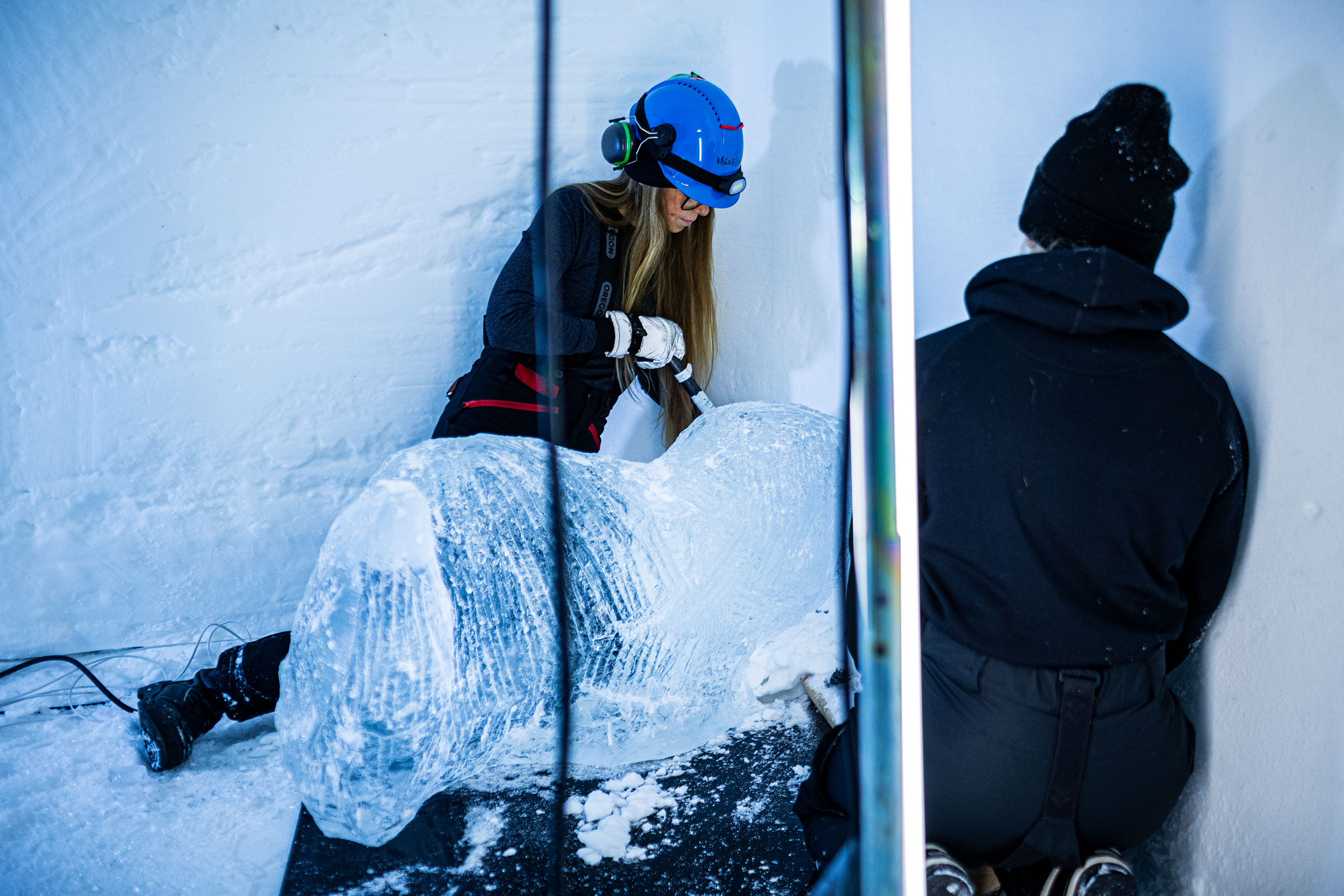 Eisbildhauerin bei der Arbeit an einer Eisskulptur mit Werkzeug und Schutzkleidung.