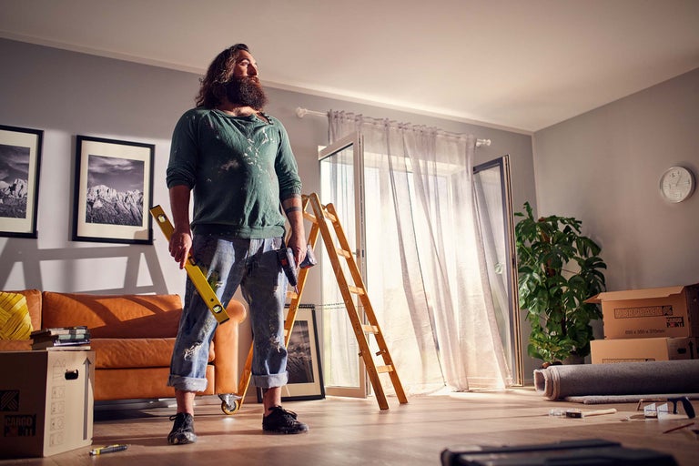 Salon avec homme, niveau à bulle, échelle, cartons de déménagement et outils pour travaux de rénovation