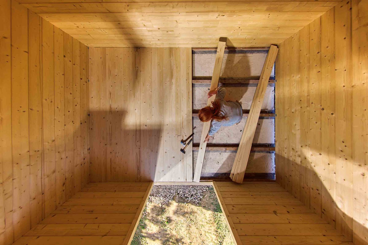 Vue intérieure d'une maison en bois avec une femme posant un plancher en bois.