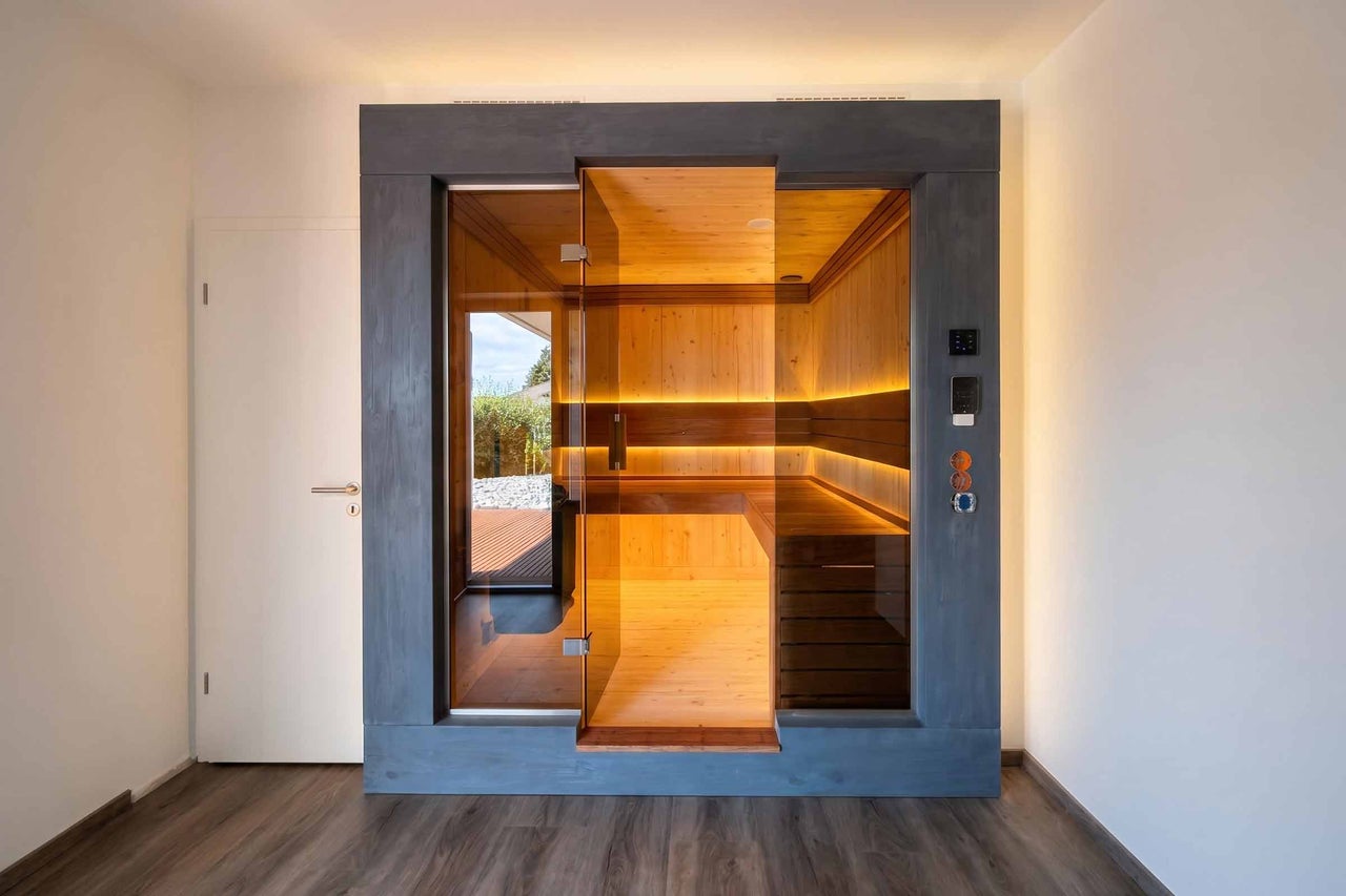 Sauna d intérieur moderne avec façade et porte en verre, intérieur en bois avec bancs de sauna et éclairage LED indirect.