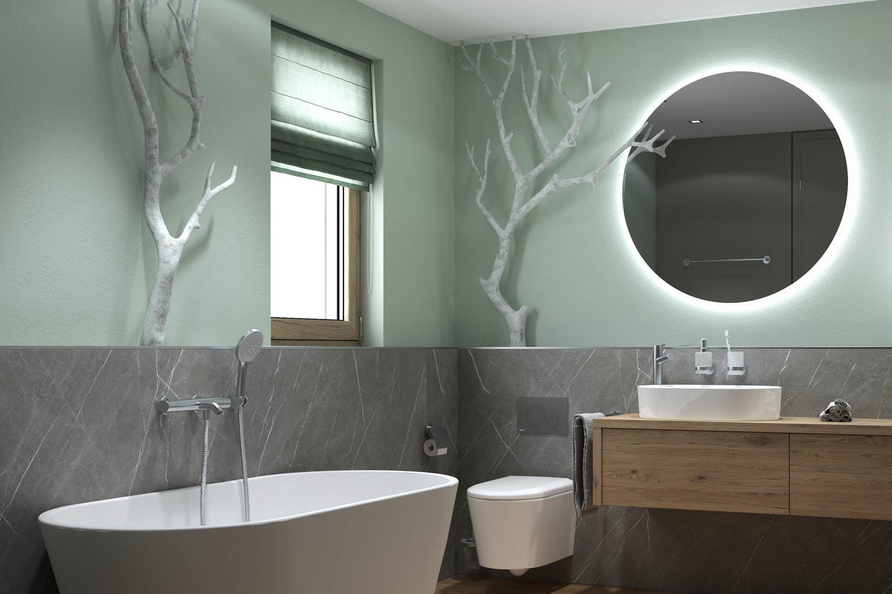 Salle de bains moderne avec baignoire îlot, toilettes suspendues et meuble en bois. Grand miroir rond avec éclairage et branches décoratives murales.
