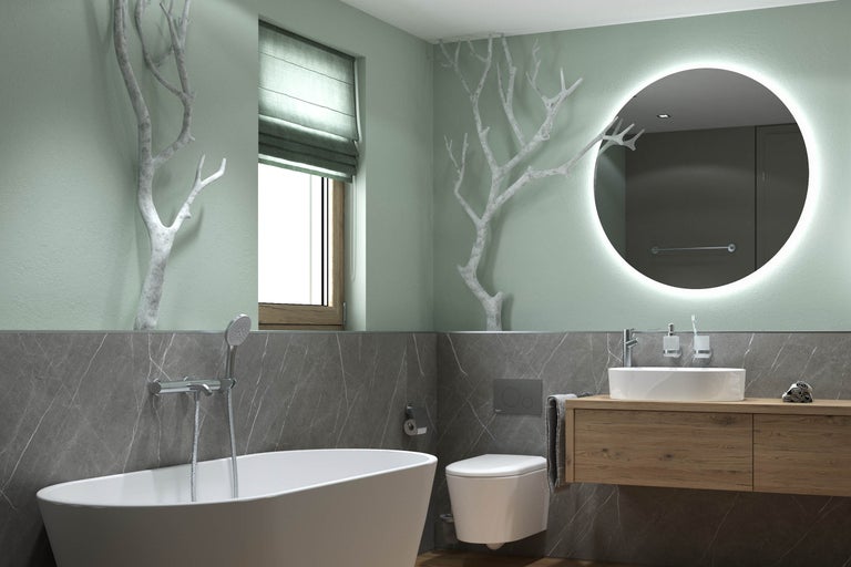 Salle de bains moderne avec baignoire îlot, toilettes suspendues et meuble en bois. Grand miroir rond avec éclairage et branches décoratives murales.