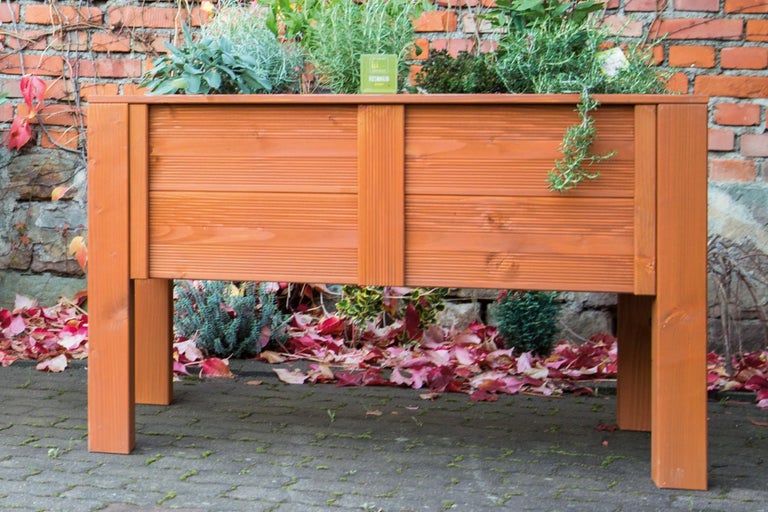 Jardinière en bois avec herbes aromatiques devant un mur de briques
