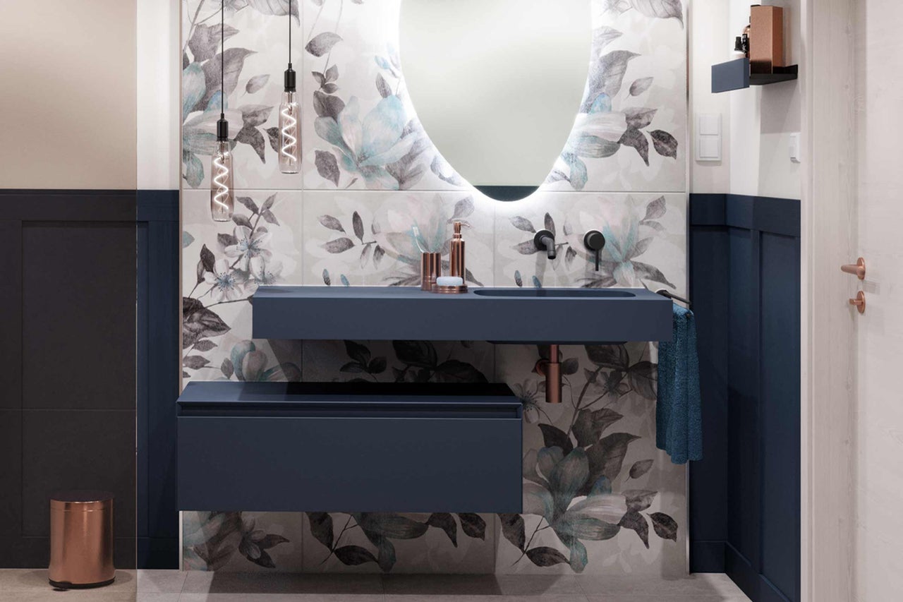 Salle de bains moderne avec meuble-lavabo bleu, miroir avec éclairage et carrelage à motifs floraux