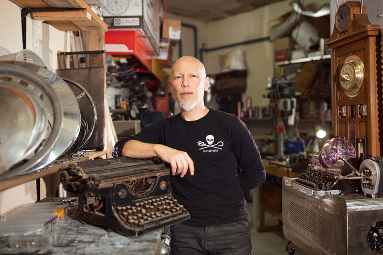 Mann in einer Werkstatt mit Vintage-Schreibmaschinen und Werkzeugen im Hintergrund