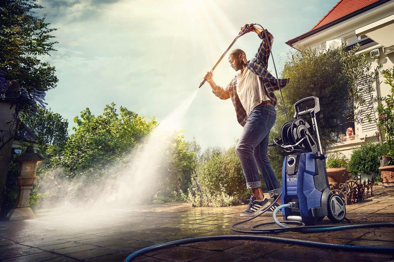 Un homme nettoie une terrasse en pierre avec un nettoyeur haute pression dans le jardin.