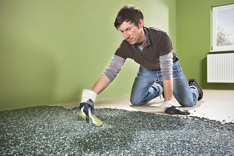 Un homme pose un tapis de pierre avec une spatule dans une pièce.